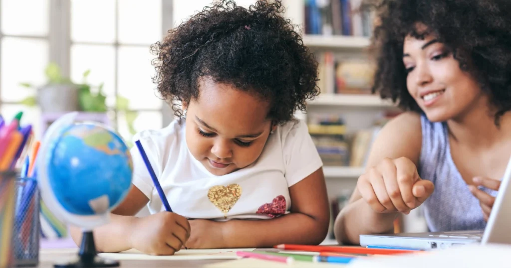 Mother watching child write in homeschool workbook at desk
