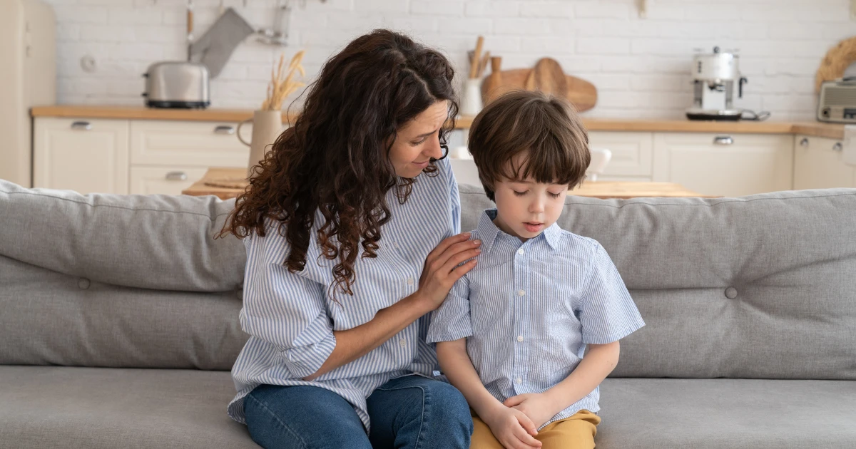 Parent comforting a young child who appears stressed after school while sitting at home