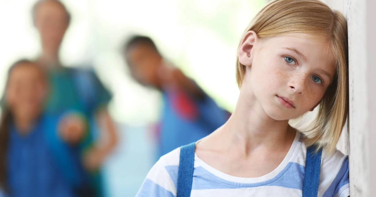 Child leaning against a wall looking sad while other children are blurred in the background
