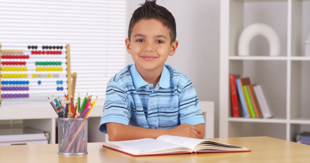 Young student smiling at desk with open textbook, pencils, and abacus in organized homeschool learning space