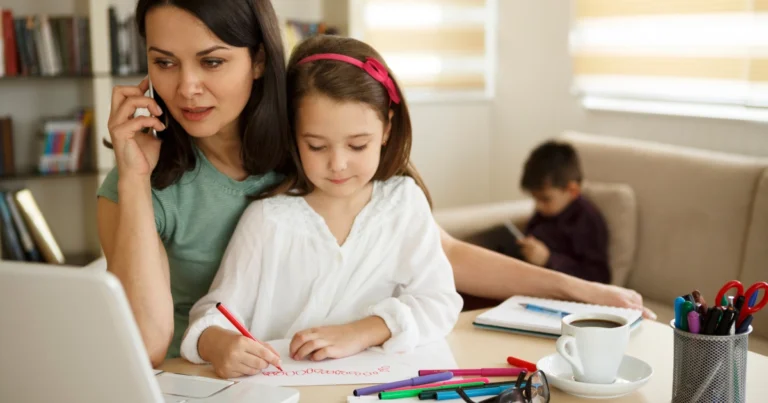 Parent on phone managing homeschool paperwork with children at home desk