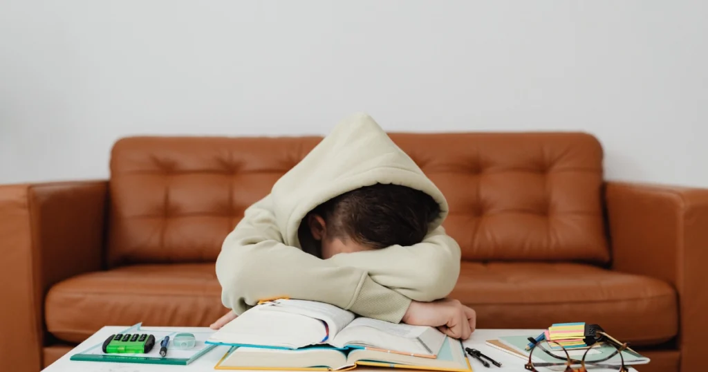 Child resting head on arms over schoolwork appearing mentally exhausted