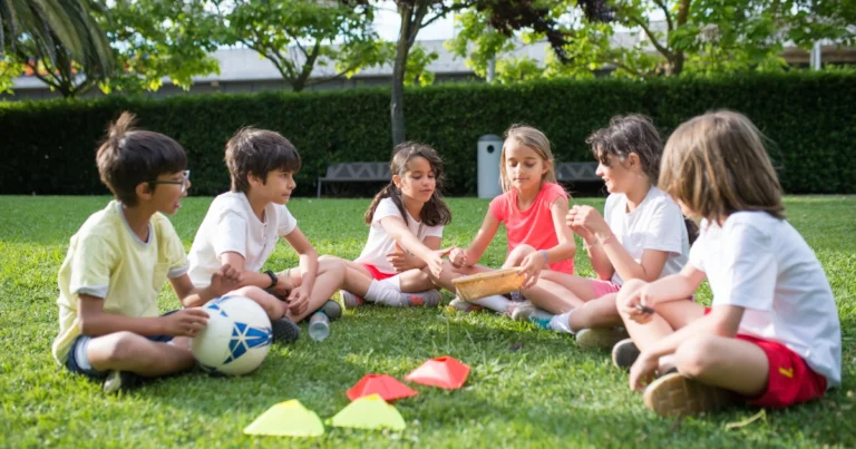 Children sitting together in a park talking and spending time together during an outdoor group activity.