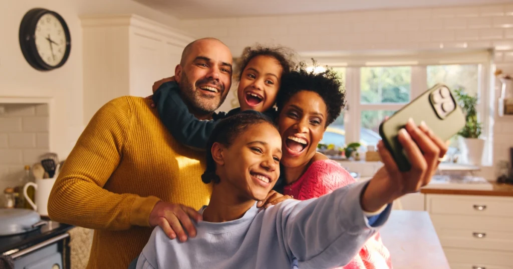 Family taking a smiling selfie together in their kitchen.