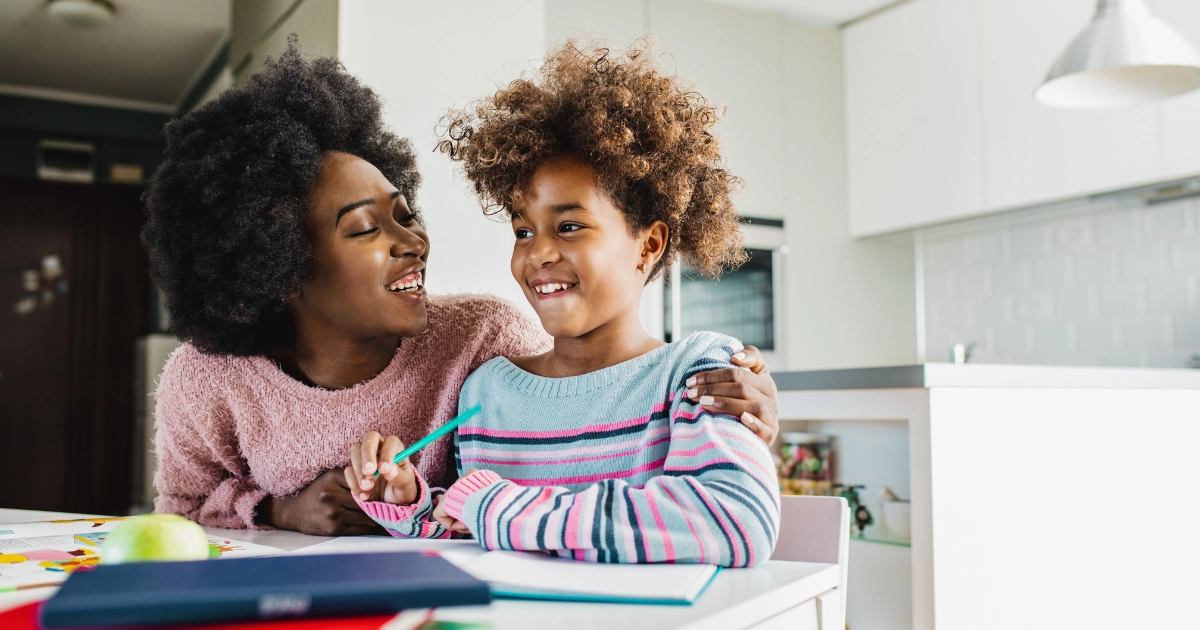 Parent encouraging a smiling child during a homeschool lesson at the kitchen table.
