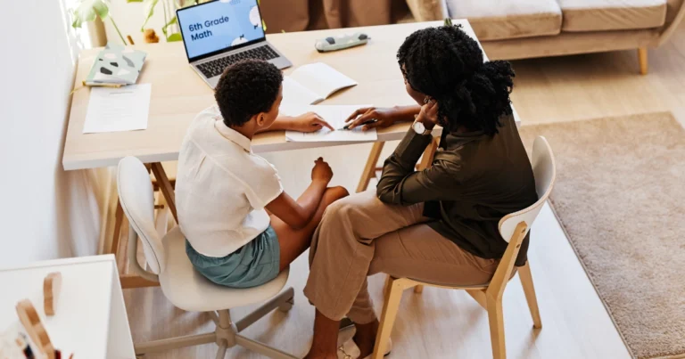 Parent homeschooling a child at a kitchen table, working together on a math lesson in a home learning environment.