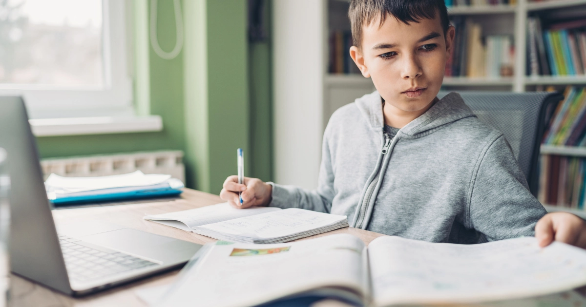 Elementary-aged homeschool student working independently at a desk while a parent provides quiet guidance nearby.